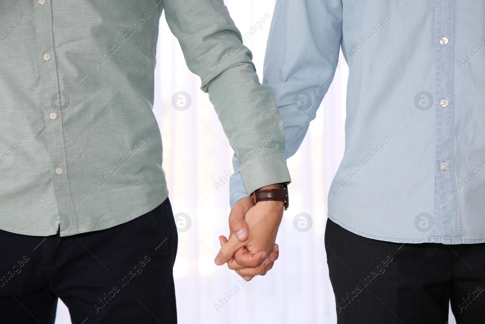 Photo of Gay couple holding hands on light background, closeup view