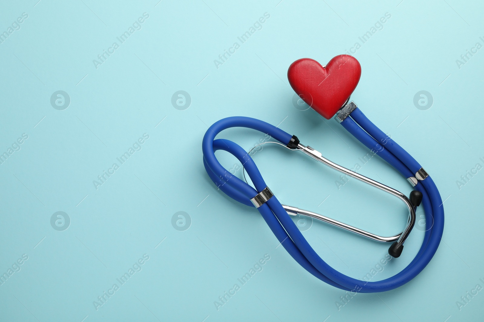 Photo of Stethoscope and red heart on light blue background, top view. Space for text