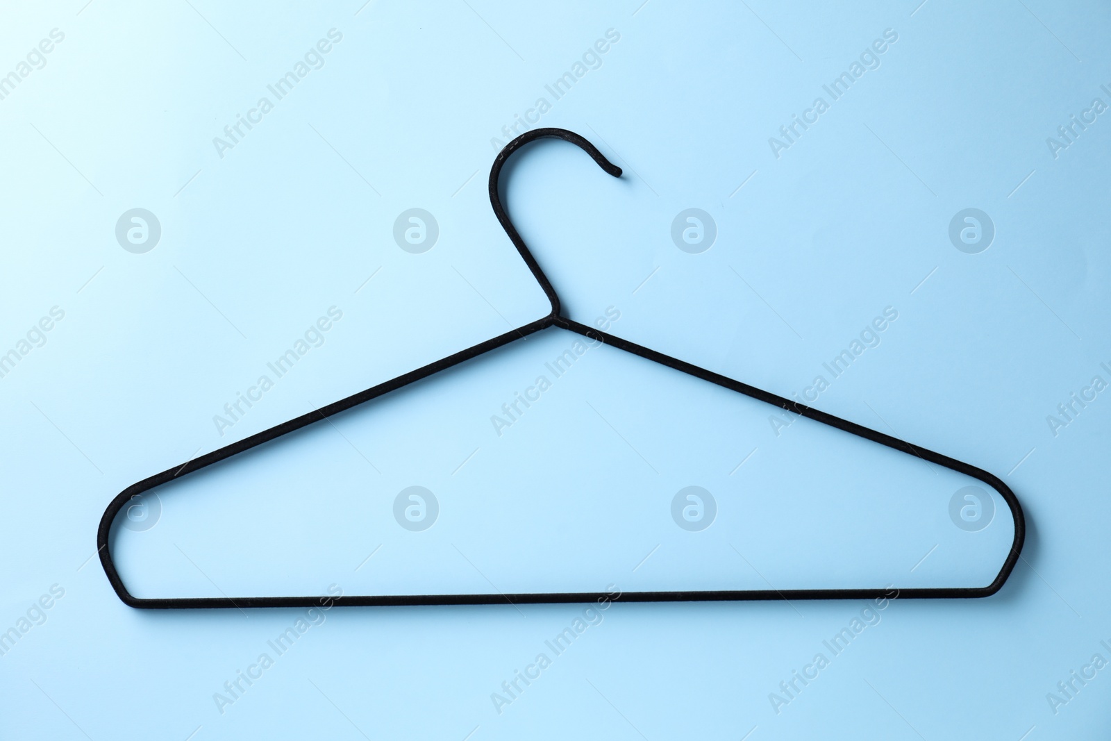Photo of One black hanger on light blue background, top view