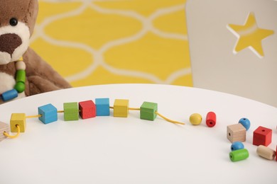 Photo of Wooden pieces and string for threading activity on white table. Motor skills development