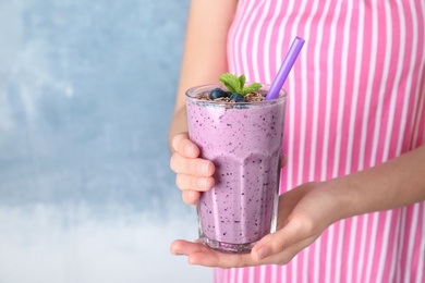 Woman holding glass of delicious blueberry smoothie on blue background, closeup. Space for text