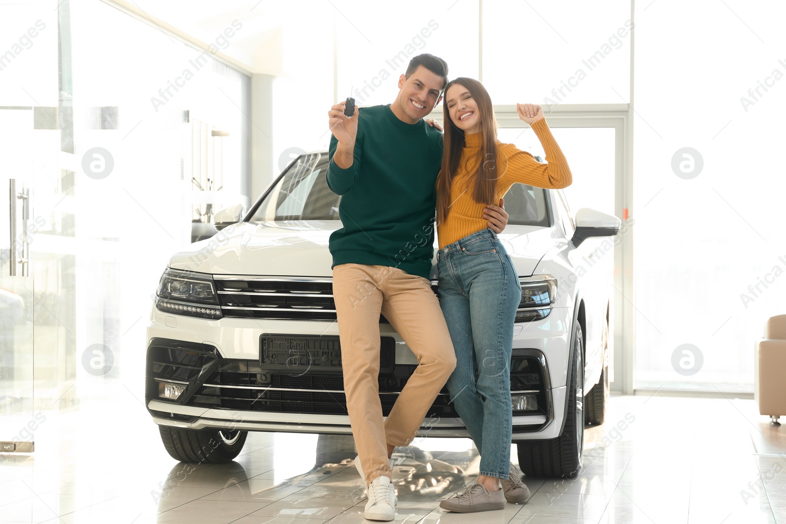 Photo of Happy couple with car key in modern auto dealership