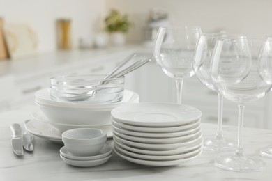 Photo of Different clean dishware, cutlery and glasses on white marble table in kitchen