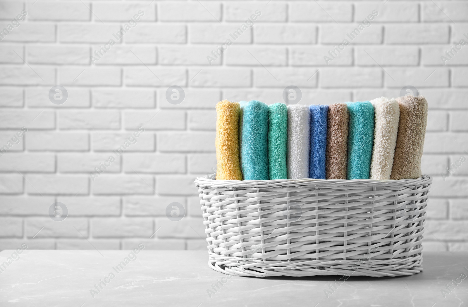 Photo of Basket with clean towels on table against brick wall background