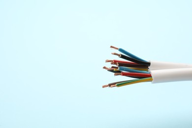 Photo of Cables with stripped wires on light blue background, closeup