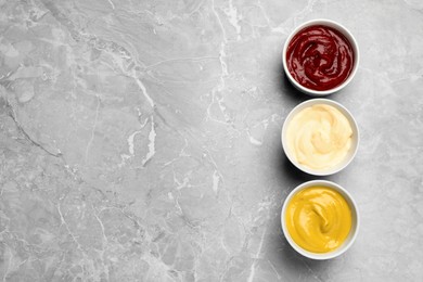 Photo of Bowls with mustard, ketchup and mayonnaise on light grey table, flat lay. Space for text