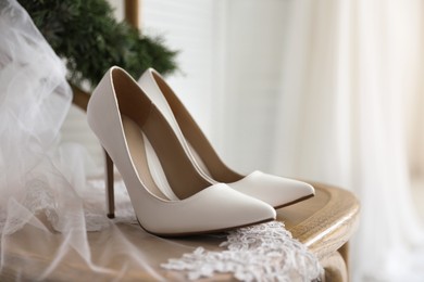 Pair of white high heel shoes, veil and wreath on wooden chair indoors. Dressing for wedding