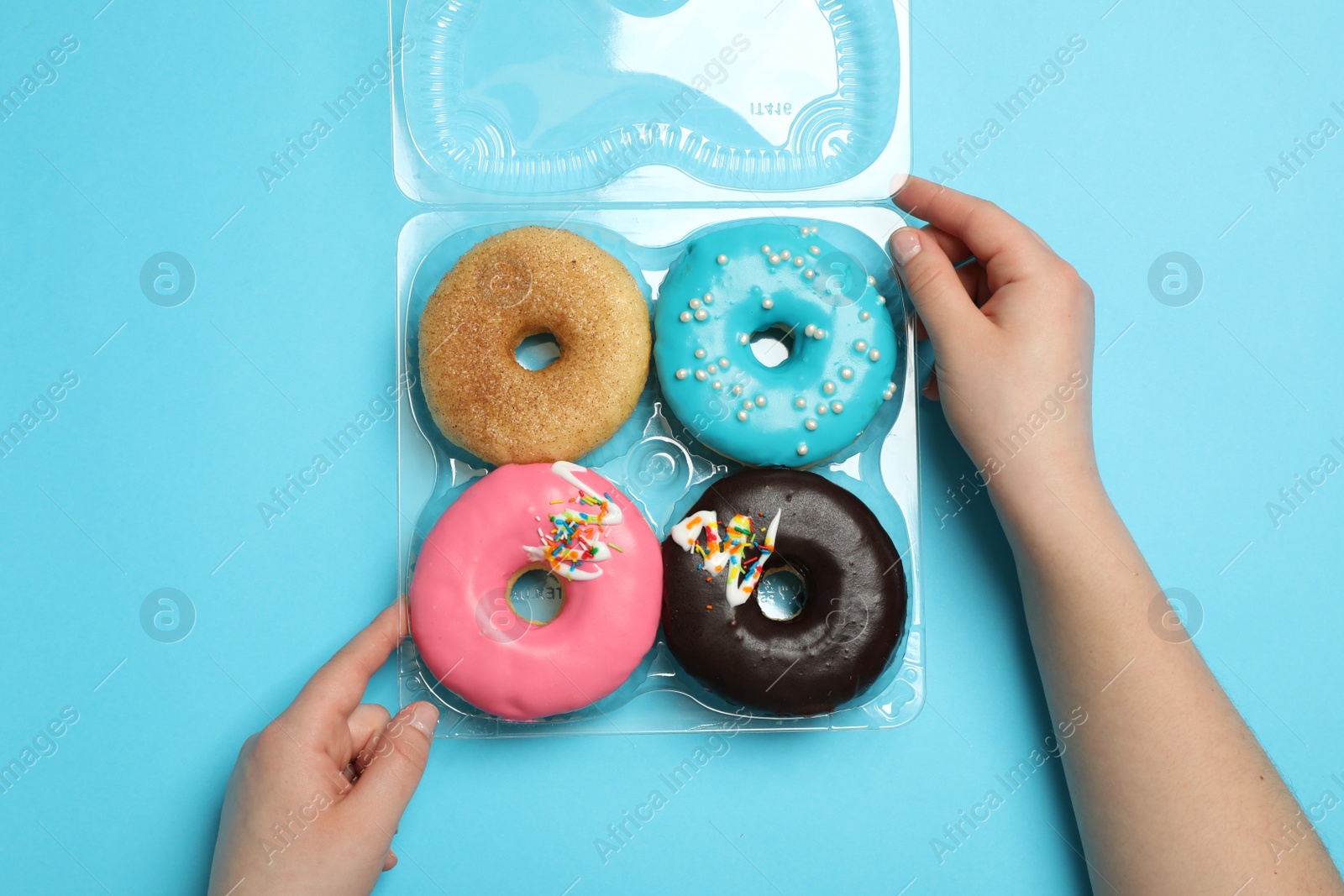 Photo of Woman with box of delicious donuts on light blue background, top view