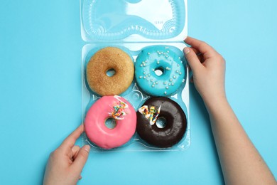 Photo of Woman with box of delicious donuts on light blue background, top view