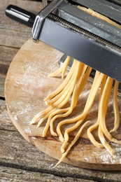 Pasta maker with raw dough on wooden table, above view