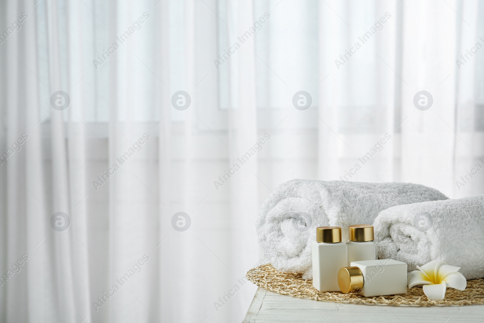 Photo of Cosmetic bottles, flower and towels on white wooden table indoors, space for text. Spa treatment