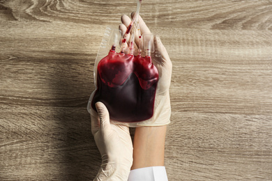 Woman holding blood for transfusion at wooden table, top view. Donation concept