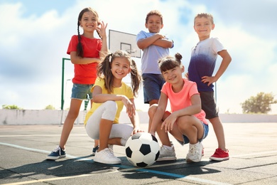 Photo of Cute children with soccer ball at sports court on sunny day. Summer camp