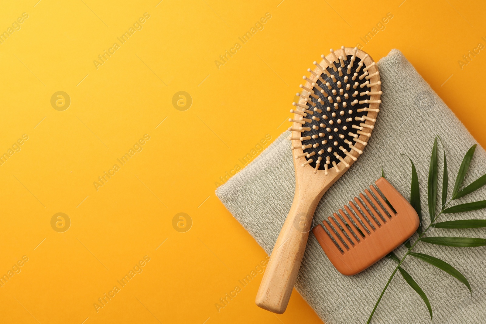 Photo of Wooden hairbrush, comb, towel and green leaves on orange background, top view. Space for text