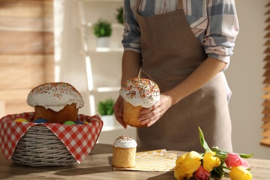 Woman putting traditional Easter cakes in basket indoors, closeup