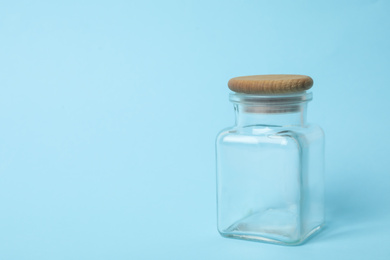 Photo of Closed empty glass jar on light blue background, space for text