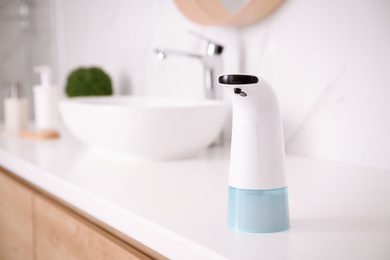 Photo of Modern automatic soap dispenser on countertop in bathroom. Space for text