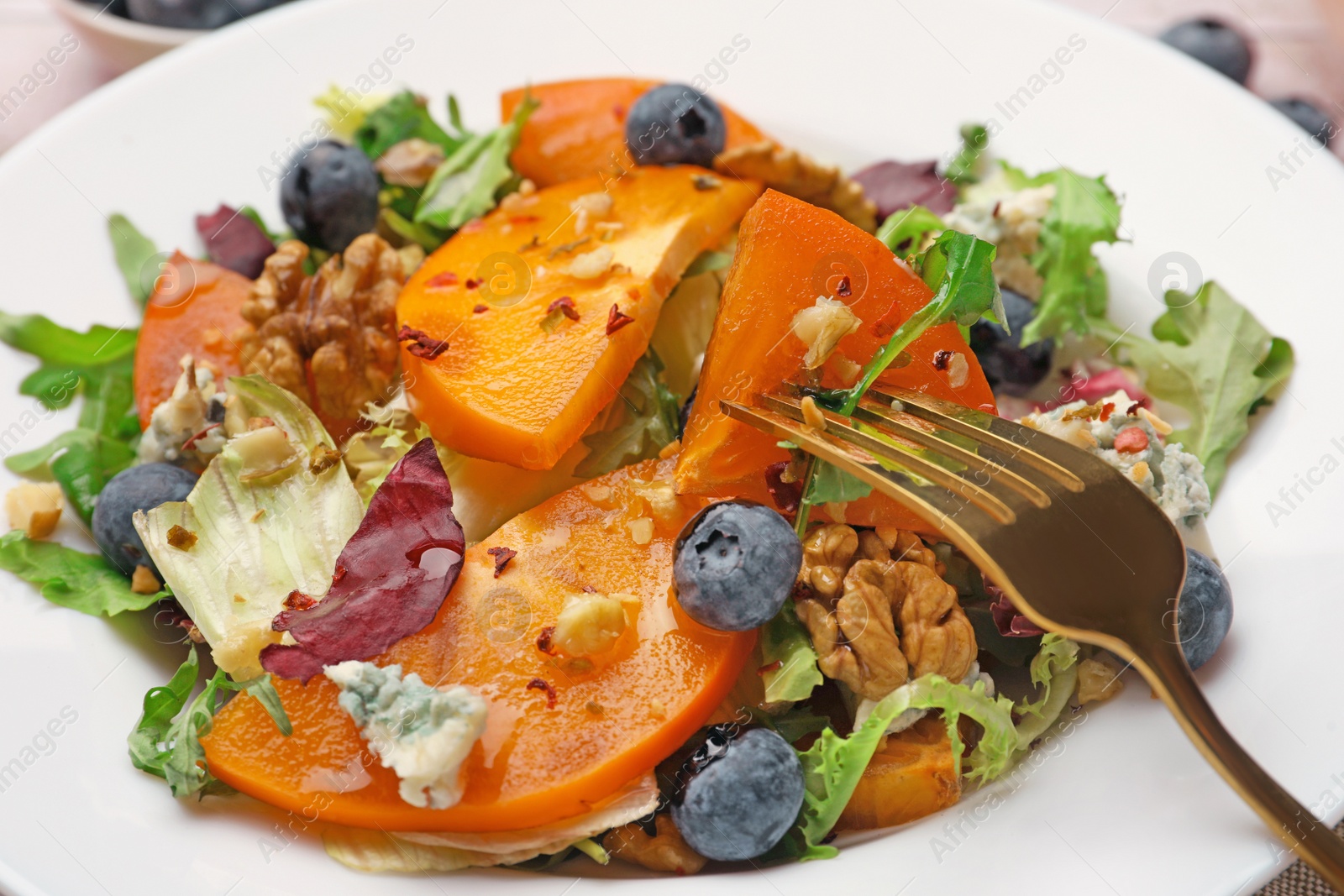 Photo of Delicious persimmon salad and fork on white plate, closeup