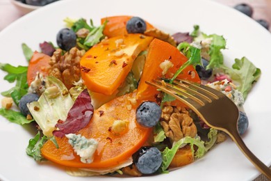 Delicious persimmon salad and fork on white plate, closeup