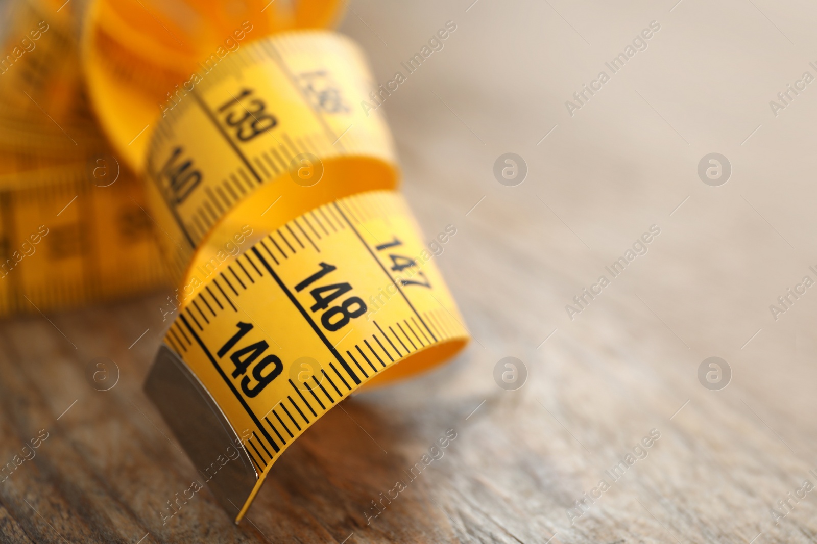 Photo of New yellow measuring tape on wooden table, closeup. Space for text