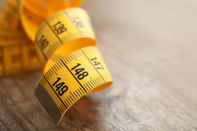 Photo of New yellow measuring tape on wooden table, closeup. Space for text