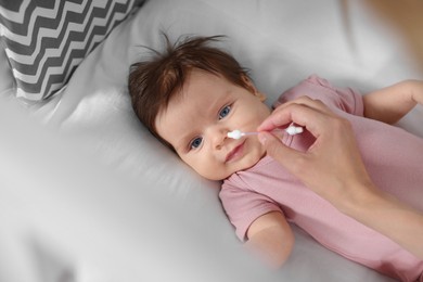 Mother cleaning nose of her baby with cotton bud on bed, closeup