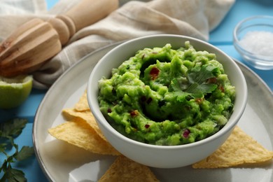Photo of Delicious guacamole served with nachos chips on light blue table, closeup