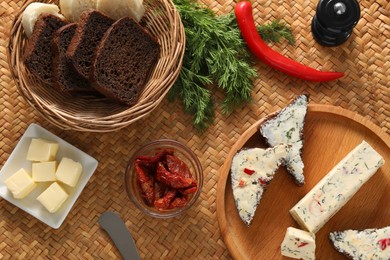 Photo of Tasty butter, dill, chili peppers and rye bread on wicker mat, flat lay