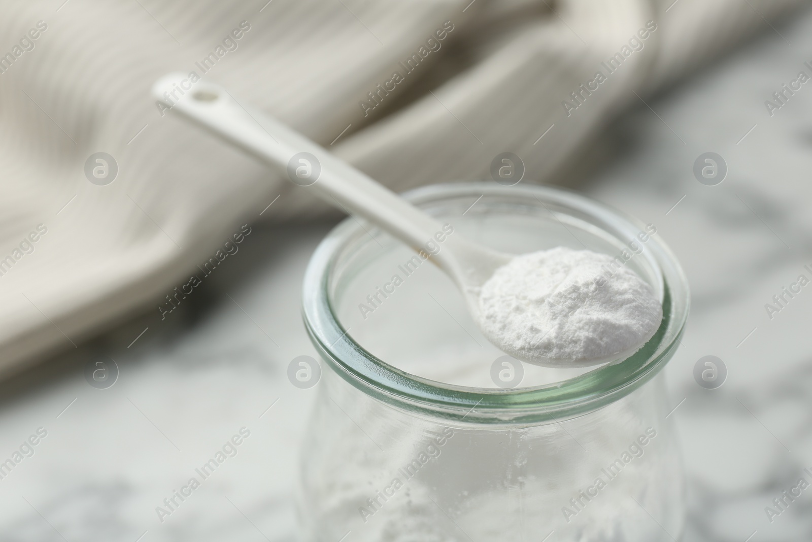 Photo of Baking powder in jar and spoon on white table, closeup. Space for text