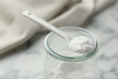 Baking powder in jar and spoon on white table, closeup. Space for text