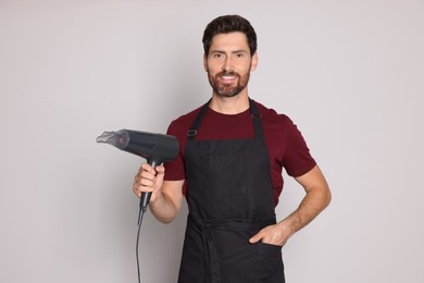Photo of Smiling hairdresser with dryer on light grey background