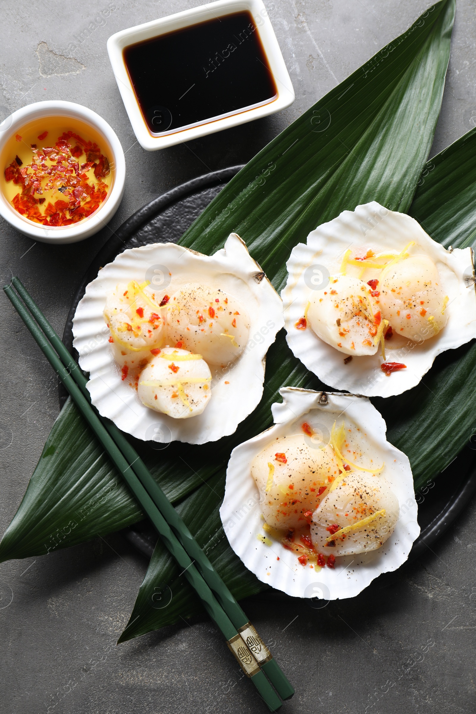 Photo of Raw scallops with spices, lemon zest, shells and sauces on grey textured table, flat lay