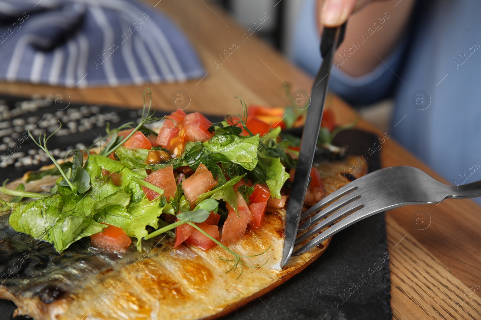 Photo of Woman eating delicious grilled fish with vegetables at wooden table, closeup