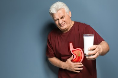 Mature man with glass of milk suffering from heartburn on color background. Stomach with hot chili pepper symbolizing acid indigestion, illustration