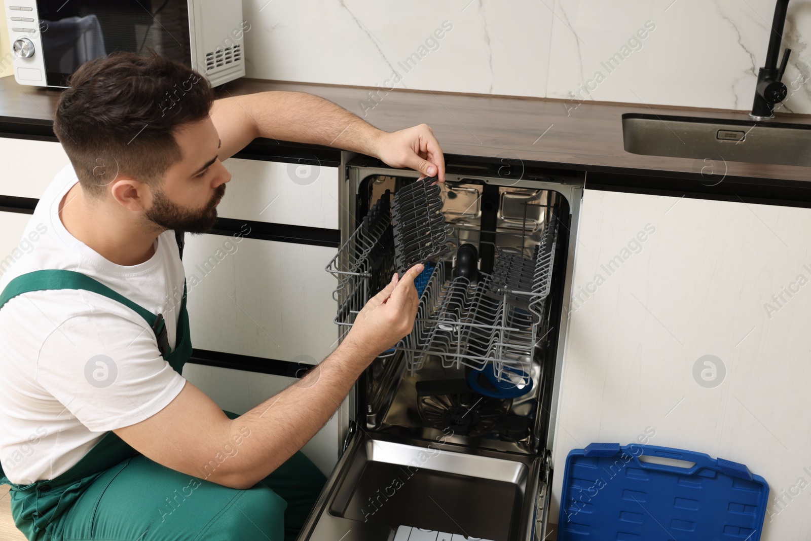 Photo of Serviceman examining dishwasher cutlery rack in kitchen