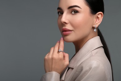 Young woman with elegant jewelry on dark grey background, closeup. Space for text