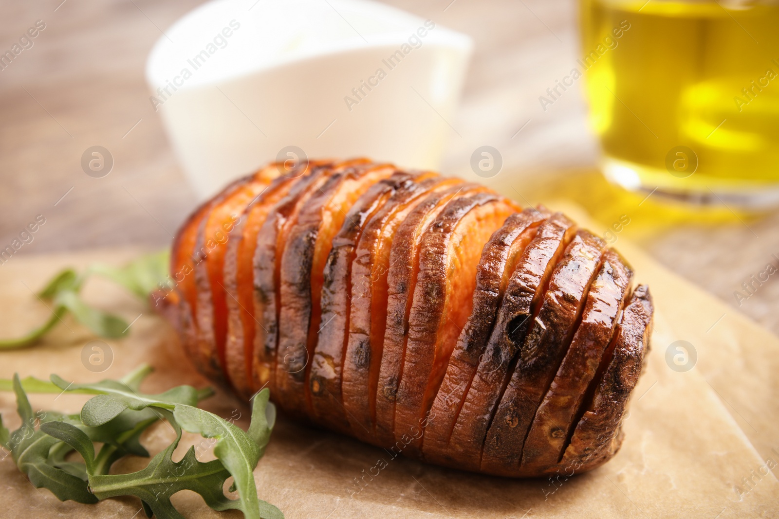 Photo of Delicious baked sweet potato and arugula on parchment, closeup