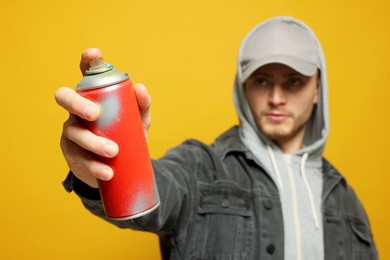 Handsome man holding can of spray paint on yellow background