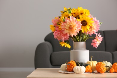 Photo of Autumn mood. Beautiful bouquet with bright flowers and small pumpkins on wooden table in room, space for text