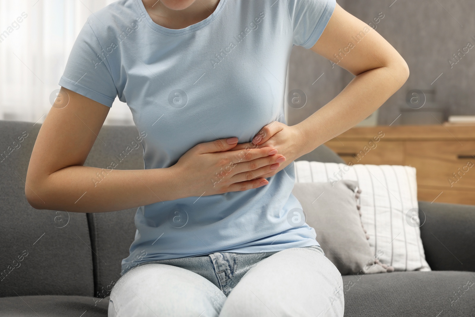 Photo of Woman suffering from stomach pain on sofa indoors, closeup