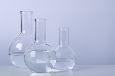 Photo of Florence flasks with transparent liquid on table against light background. Space for text