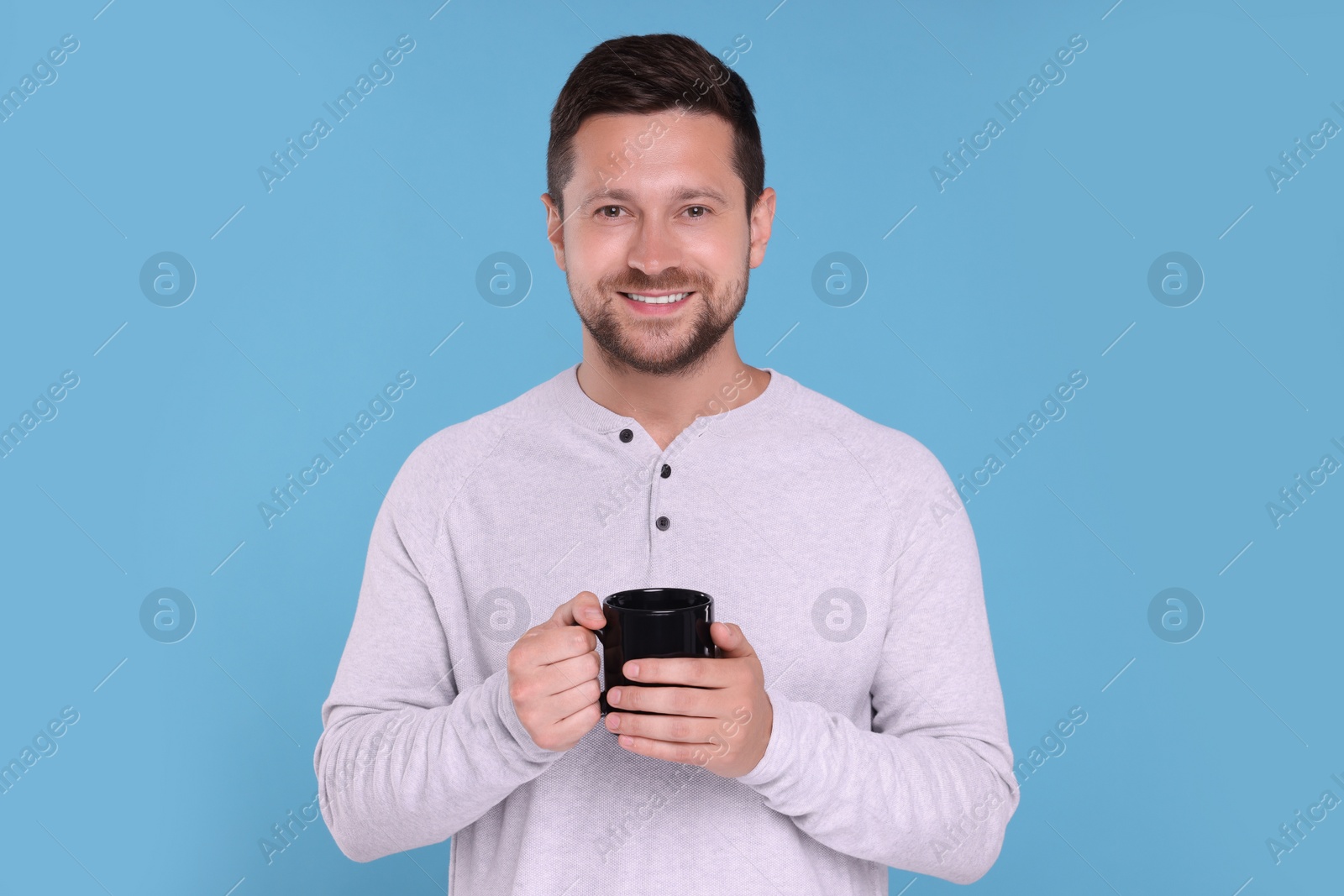 Photo of Portrait of happy man holding black mug on light blue background