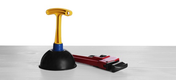 Photo of Plunger with plastic handle and pipe wrench on white table