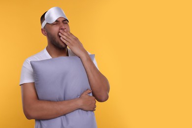 Photo of Tired man with pillow and sleep mask yawning on orange background, space for text. Insomnia problem