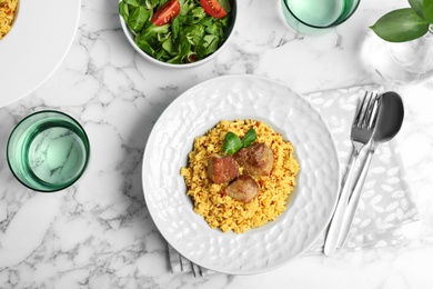 Photo of Delicious rice pilaf with salad served on marble table, flat lay