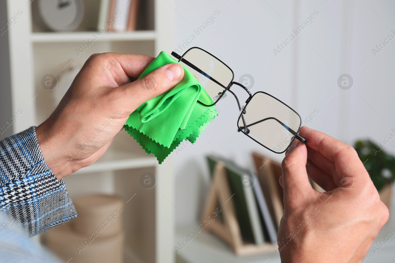 Photo of Man wiping glasses with microfiber cloth indoors, closeup