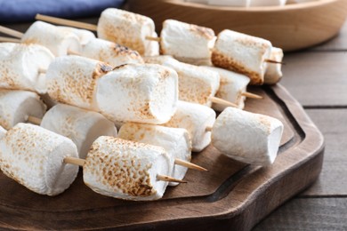 Photo of Sticks with roasted marshmallows on wooden table, closeup