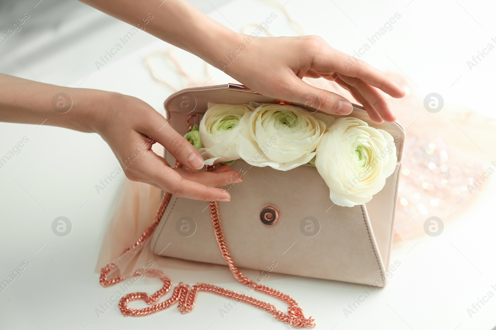 Photo of Woman holding stylish clutch bag with spring flowers on light table, closeup