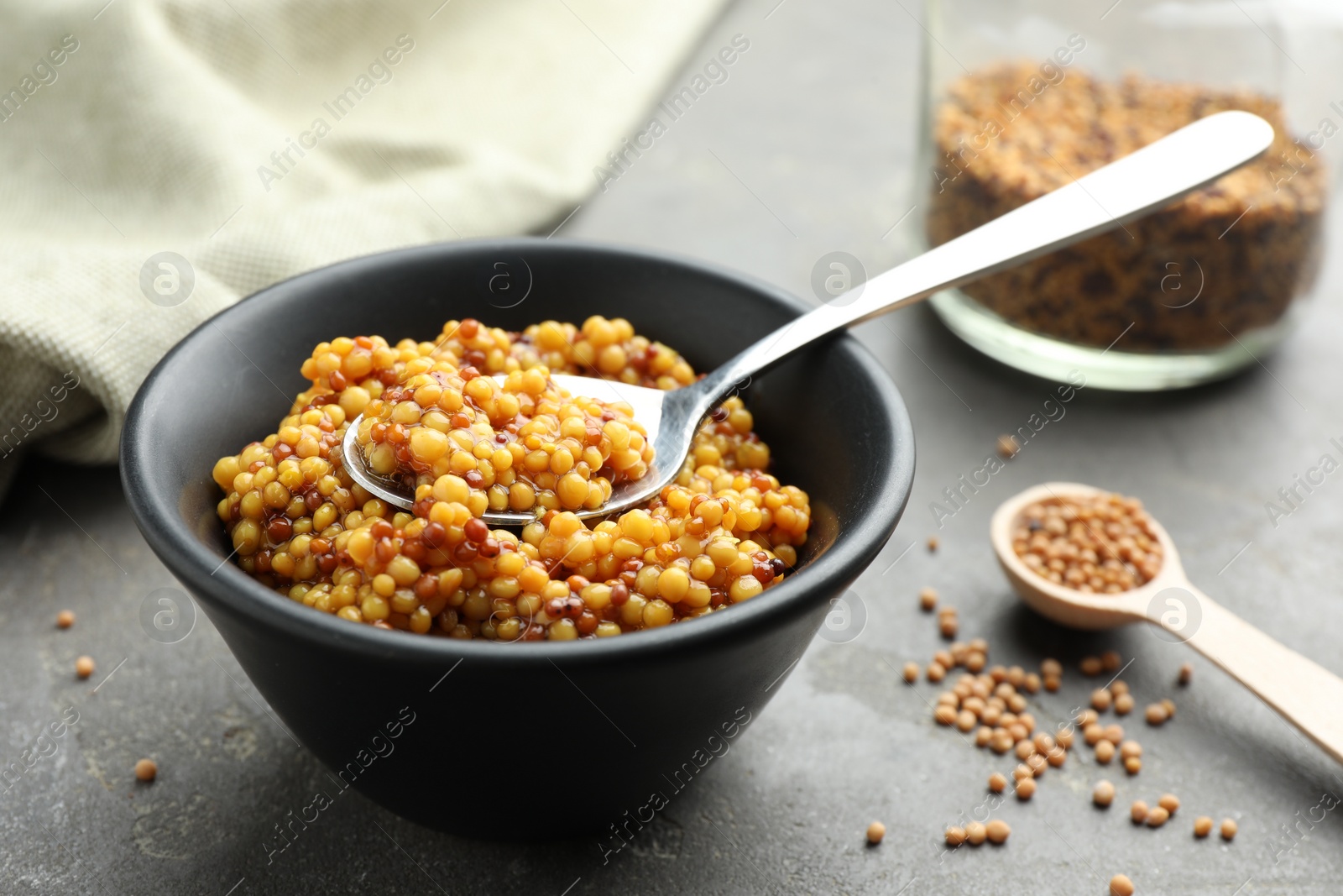 Photo of Whole grain mustard in bowl, spoon and dry seeds on grey table