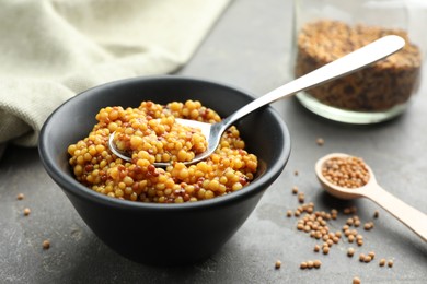 Photo of Whole grain mustard in bowl, spoon and dry seeds on grey table